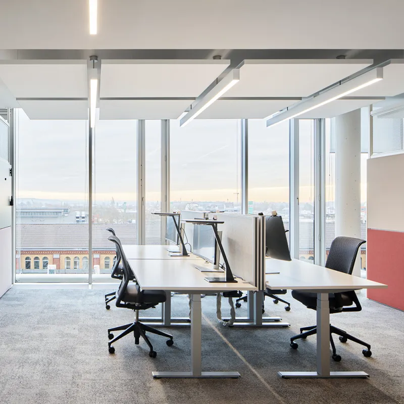 Stadtwerke_Deudo_Helles Büro mit höhenverstellbaren Schreibtischen, ergonomischen Stühlen, Teppichboden und Stadtblick.