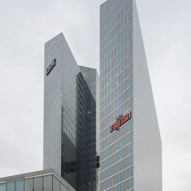 Fish & Richardson Moderne Glashochhäuser mit den Logos von IBM und Fujitsu ragen in den Himmel unter bewölktem Himmel.